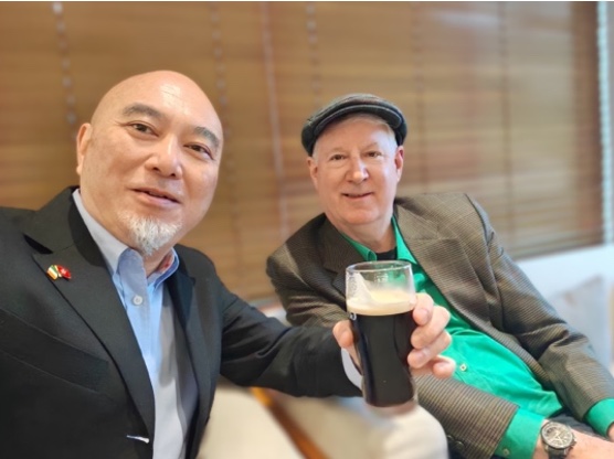 Two men smiling, one holding a pint of stout