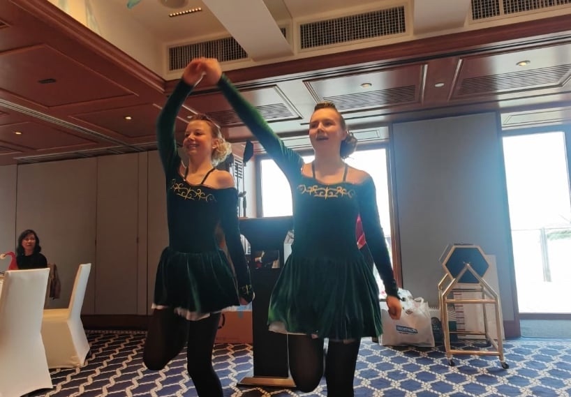 Two Irish dancers in green dresses performing in a dining room