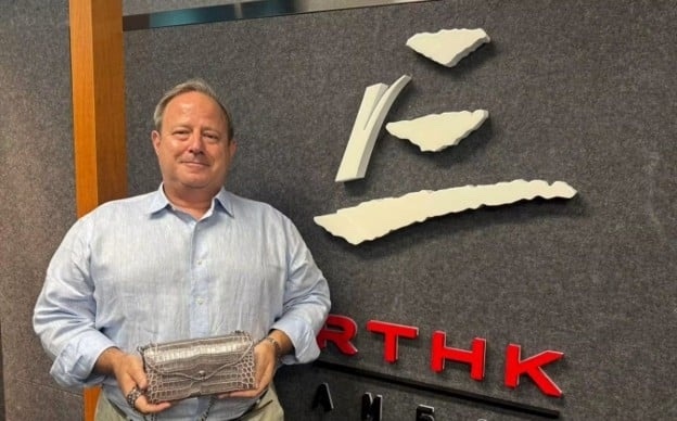 A man holding a leather bag beside the RTHK sign