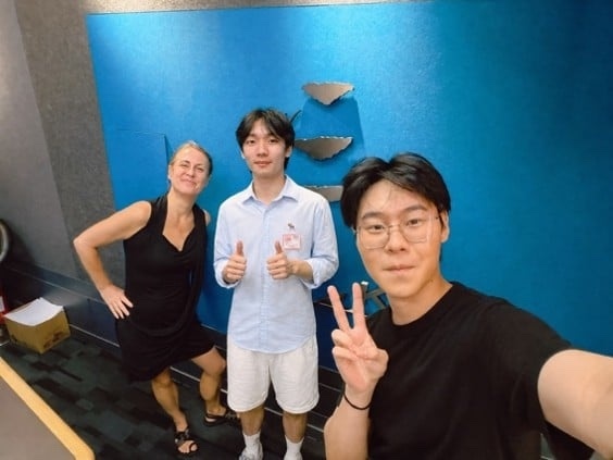 Three people smiling in a radio station corridor in front of a blue wall