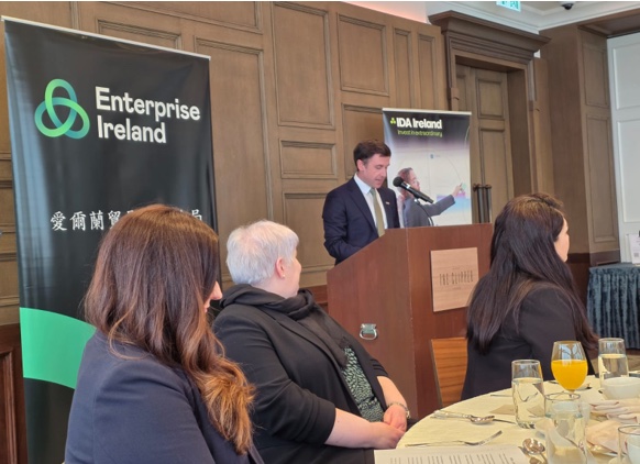 A speaker at a lectern before Enterprise Ireland and IDA Ireland banners, guests at lunch