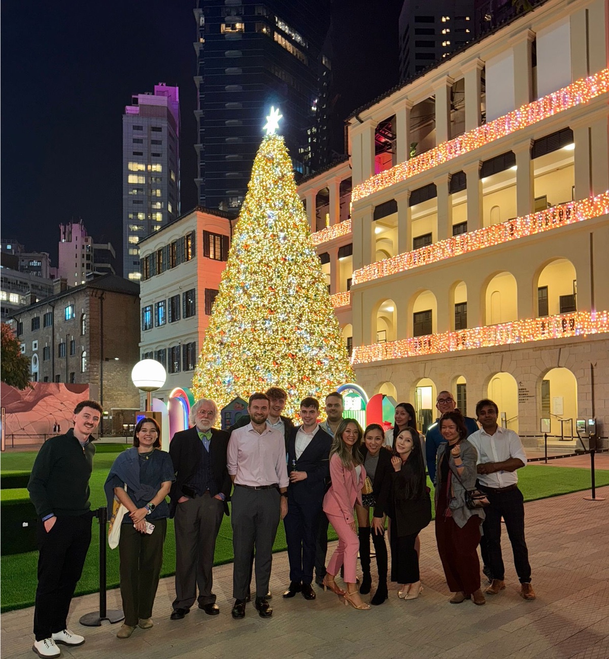 Young professionals gathered in front of a tall lit Christmas tree at night